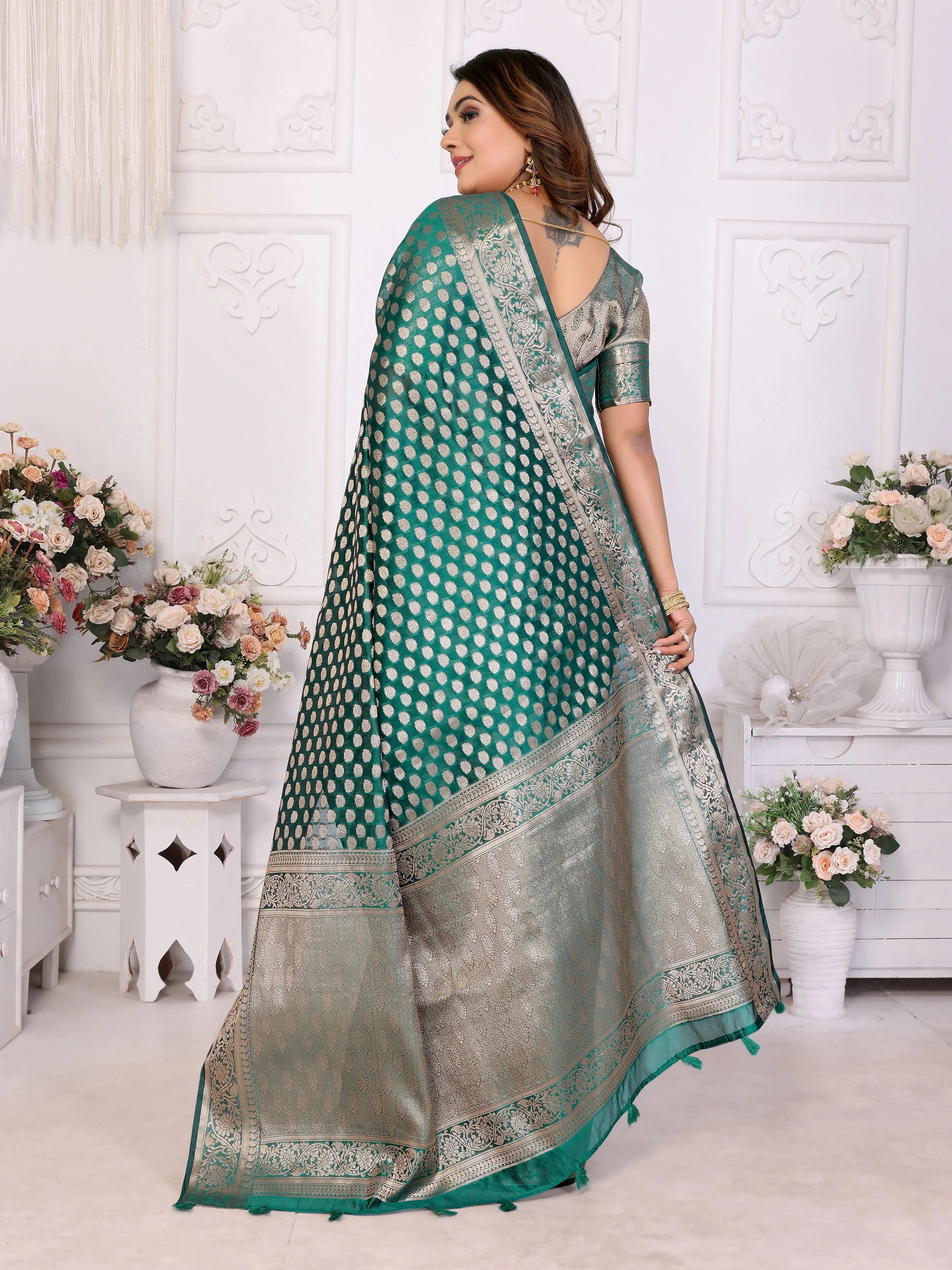 Woman wearing a green and silver saree in a decorated room with flowers.